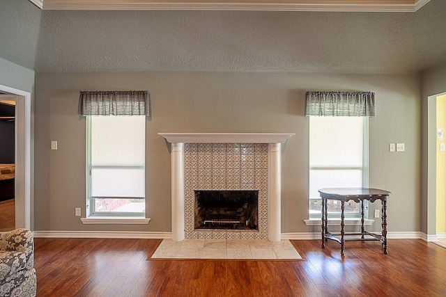 unfurnished living room with a textured ceiling, a tiled fireplace, wood finished floors, and baseboards