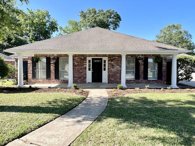 view of front facade featuring a shingled roof, covered porch, brick siding, and a front lawn