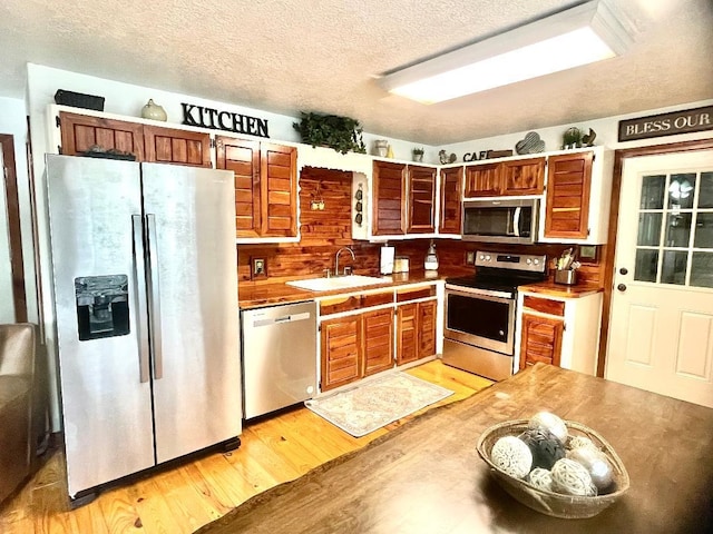 kitchen featuring appliances with stainless steel finishes, light wood-type flooring, a textured ceiling, and sink