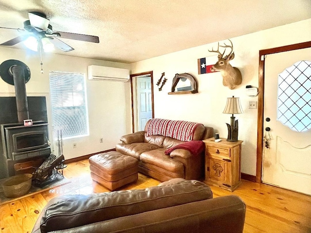 living room with a wood stove, ceiling fan, a wall unit AC, a textured ceiling, and light wood-type flooring