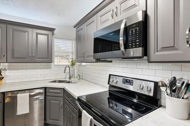 kitchen with stainless steel appliances, sink, gray cabinetry, and decorative backsplash