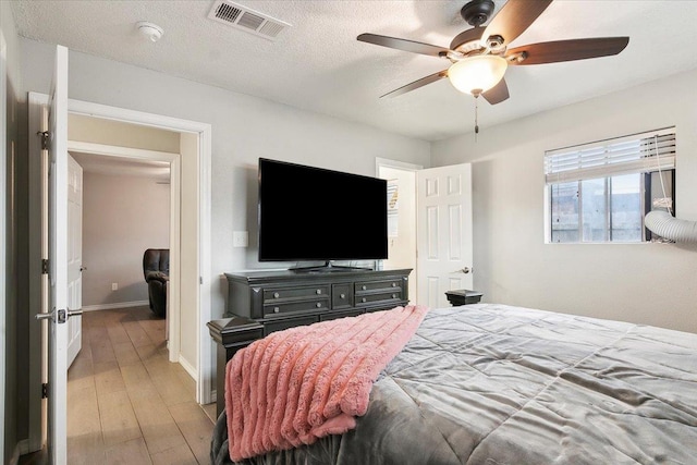 bedroom with ceiling fan, light hardwood / wood-style floors, and a textured ceiling