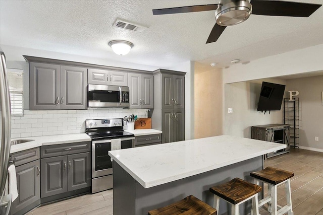 kitchen with gray cabinets, appliances with stainless steel finishes, a breakfast bar, and decorative backsplash