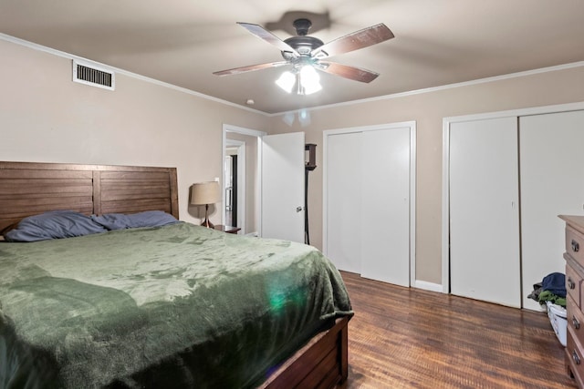 bedroom with wood finished floors, visible vents, ceiling fan, ornamental molding, and two closets