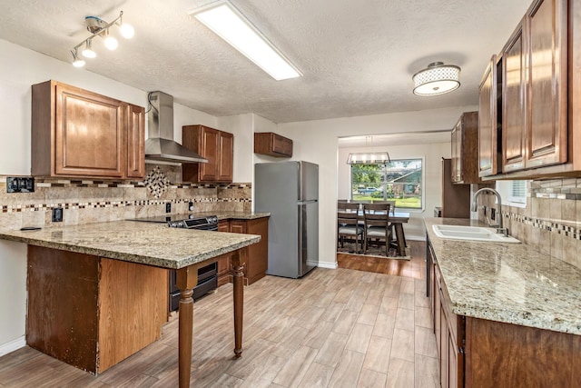 1385 Howell St, Beaumont, TX 77706 - kitchen featuring appliances with stainless steel finishes, wall chimney range hood, light wood finished floors, tasteful backsplash, and a textured ceiling