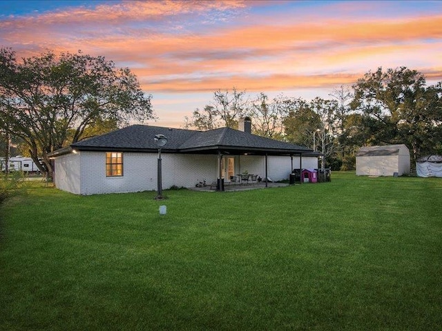 back house at dusk featuring a patio area, a shed, and a yard