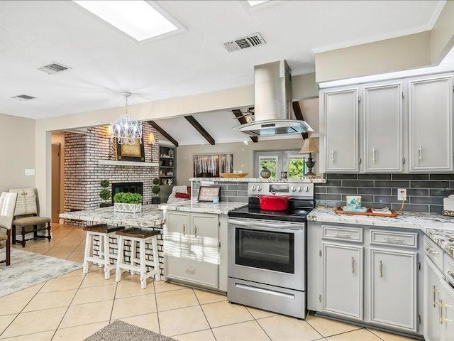 kitchen featuring island exhaust hood, light tile patterned floors, stainless steel electric stove, and a fireplace