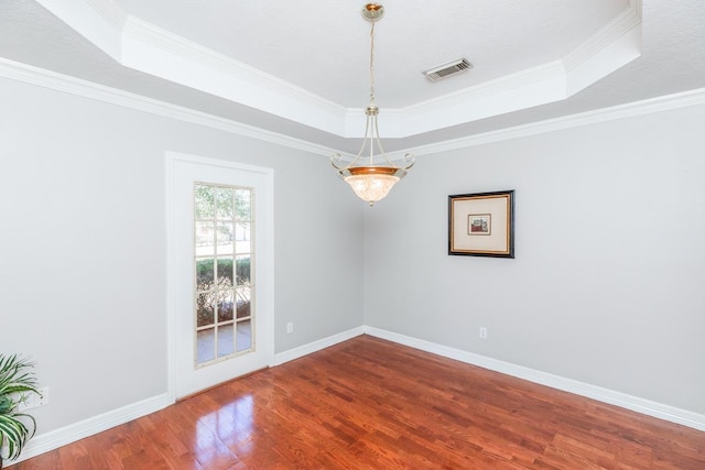 empty room featuring a raised ceiling, ornamental molding, and wood-type flooring