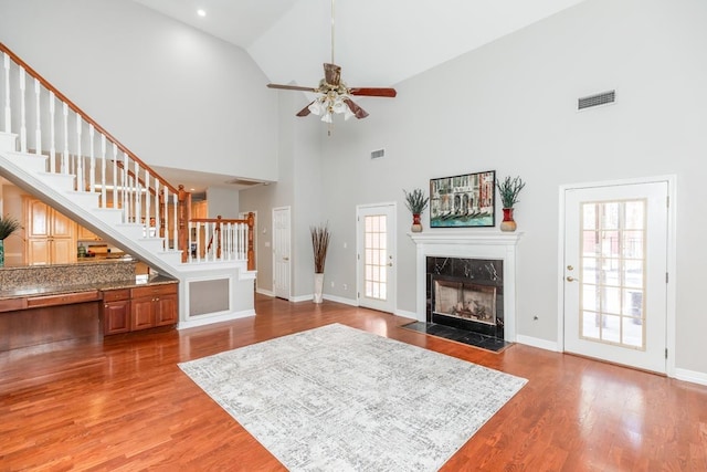 living room featuring ceiling fan, wood-type flooring, a fireplace, and a high ceiling