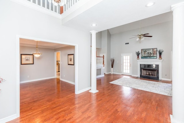 unfurnished living room with ornate columns, ceiling fan, a high ceiling, hardwood / wood-style floors, and a fireplace