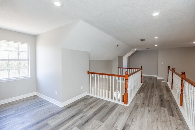 corridor with light hardwood / wood-style floors, a textured ceiling, and vaulted ceiling