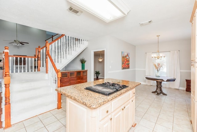 kitchen with ceiling fan with notable chandelier, light tile patterned floors, decorative light fixtures, black gas cooktop, and a center island