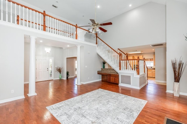 unfurnished living room with ornate columns, ceiling fan, light hardwood / wood-style flooring, and a high ceiling