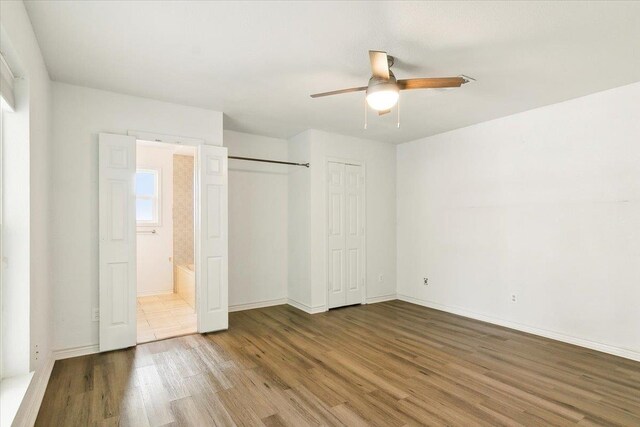 unfurnished bedroom featuring hardwood / wood-style floors, ceiling fan, and ensuite bath