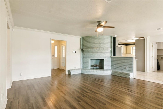 unfurnished living room featuring hardwood / wood-style flooring, a brick fireplace, ceiling fan, and crown molding