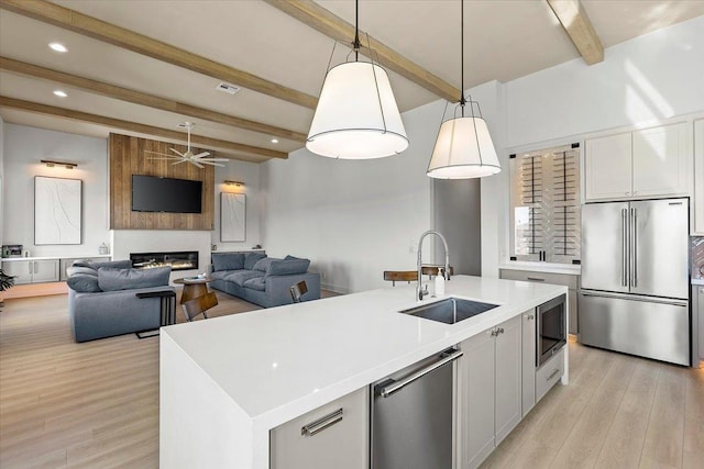 kitchen with hanging light fixtures, stainless steel appliances, beamed ceiling, an island with sink, and white cabinets