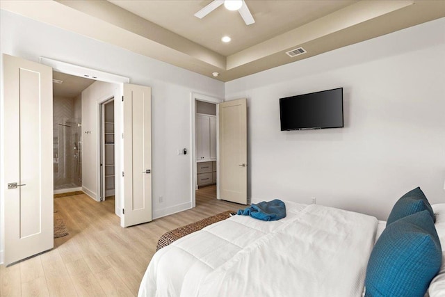 bedroom with a raised ceiling, connected bathroom, ceiling fan, and light hardwood / wood-style flooring