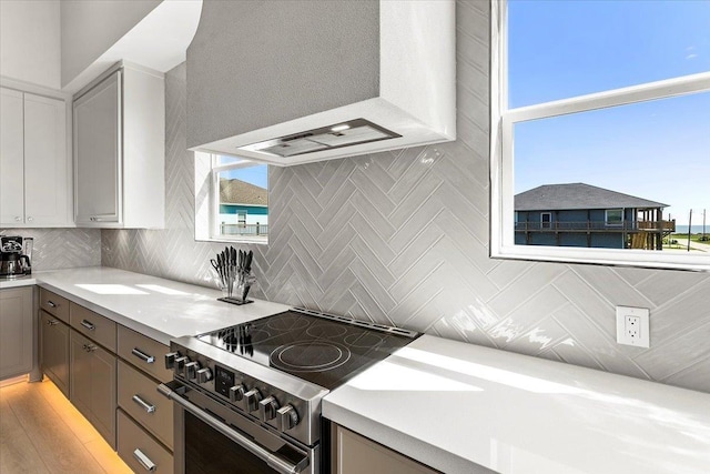 kitchen featuring light hardwood / wood-style flooring, range hood, high end stove, gray cabinets, and decorative backsplash