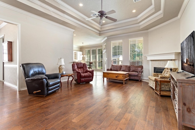 living room featuring a tray ceiling, ceiling fan, crown molding, and a tiled fireplace