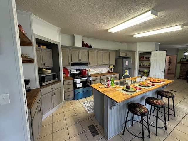 kitchen with sink, wood counters, a kitchen breakfast bar, backsplash, and appliances with stainless steel finishes