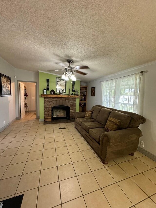 living room featuring ceiling fan, a stone fireplace, crown molding, a textured ceiling, and light tile patterned flooring