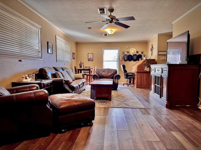 living room featuring ceiling fan, light wood-type flooring, a textured ceiling, and ornamental molding