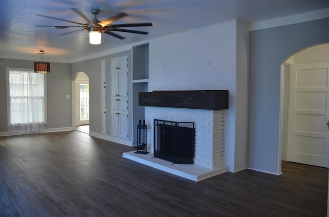 unfurnished living room with dark wood-type flooring, crown molding, a brick fireplace, ceiling fan, and a textured ceiling