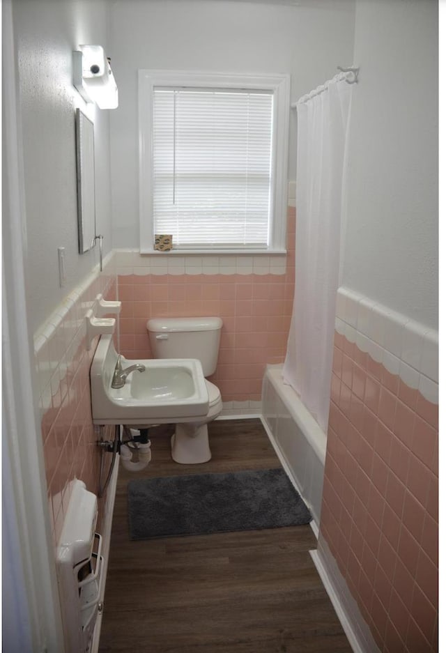 full bathroom featuring sink, shower / bathtub combination with curtain, wood-type flooring, toilet, and tile walls