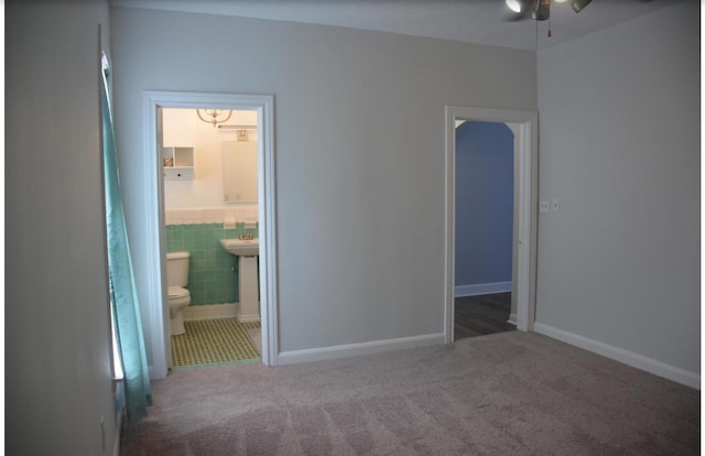 unfurnished bedroom featuring ensuite bathroom, dark carpet, and tile walls