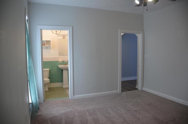 unfurnished bedroom with connected bathroom, tile walls, and dark colored carpet