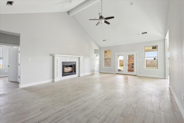 unfurnished living room with beam ceiling, a tile fireplace, french doors, ceiling fan, and light hardwood / wood-style floors