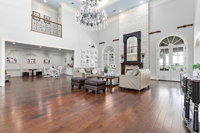 living room with french doors, a stone fireplace, dark hardwood / wood-style floors, crown molding, and a towering ceiling