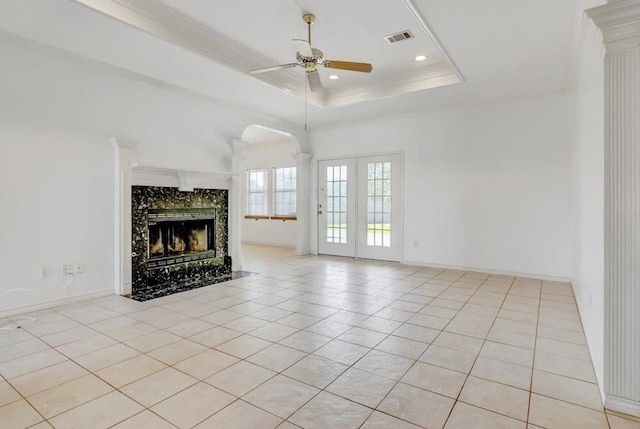 unfurnished living room with light tile patterned floors, crown molding, ceiling fan, a tray ceiling, and a fireplace