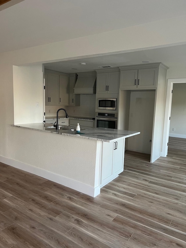 100 Country Club Dr, Beaumont, TX 77705 - kitchen featuring custom exhaust hood, baseboards, a sink, light wood-style flooring, and stainless steel appliances