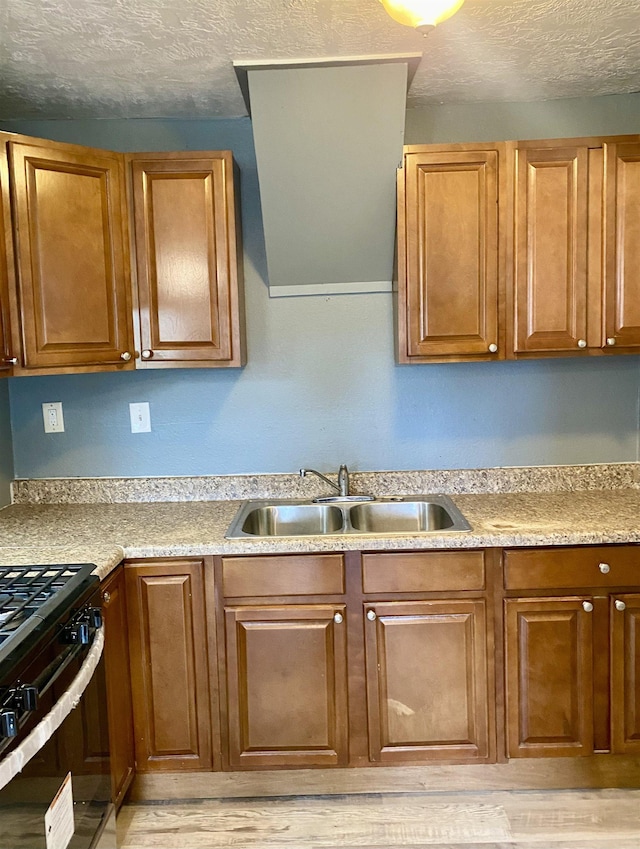 kitchen featuring gas range, sink, a textured ceiling, and light wood-type flooring