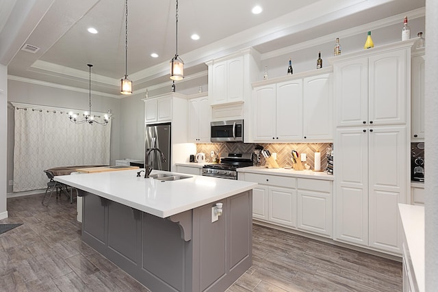 7495 Broussard Rd, Beaumont, TX 77713 - kitchen with stainless steel appliances, an island with sink, crown molding, a tray ceiling, and white cabinetry