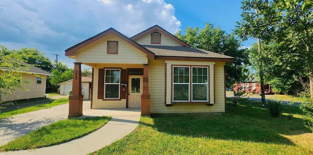 bungalow-style home featuring a front yard, a garage, an outdoor structure, and covered porch