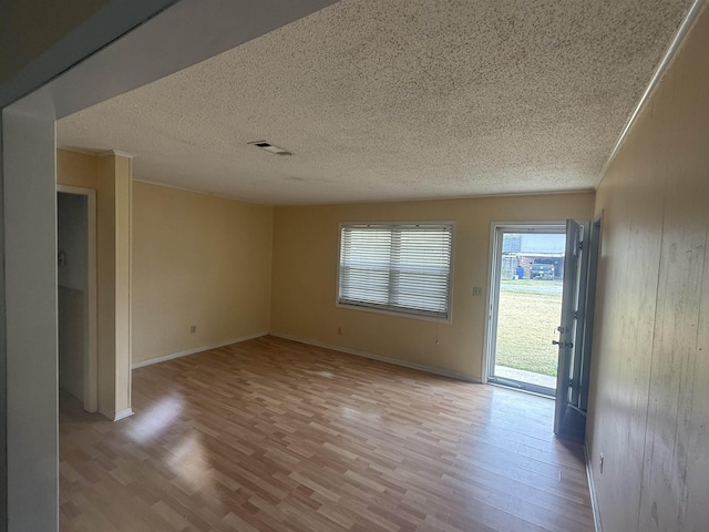 spare room with light wood-style floors, baseboards, visible vents, and a textured ceiling