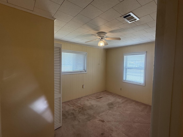 carpeted empty room featuring ceiling fan, wood walls, plenty of natural light, and visible vents