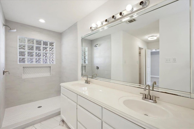 full bath featuring double vanity, visible vents, tiled shower, marble finish floor, and a sink