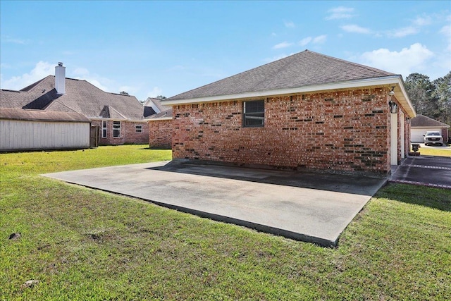 rear view of property with a patio area, a shingled roof, a lawn, and brick siding