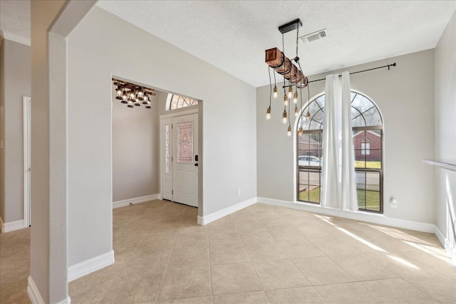 unfurnished dining area with a textured ceiling, light tile patterned flooring, a notable chandelier, visible vents, and baseboards