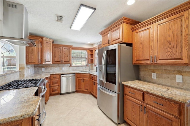 kitchen featuring visible vents, appliances with stainless steel finishes, brown cabinets, range hood, and a sink