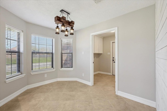 spare room with a chandelier, light tile patterned floors, a textured ceiling, and baseboards