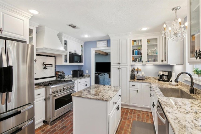 5880 Longwood St, Beaumont, TX 77707 - kitchen featuring appliances with stainless steel finishes, a sink, custom range hood, brick floors, and white cabinets