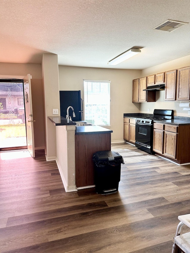 kitchen with black gas range, dark wood-type flooring, a textured ceiling, and refrigerator