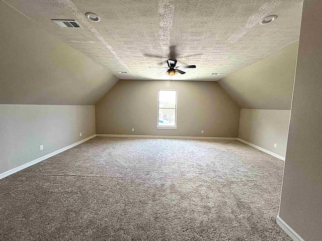 additional living space featuring a textured ceiling, carpet floors, visible vents, baseboards, and vaulted ceiling