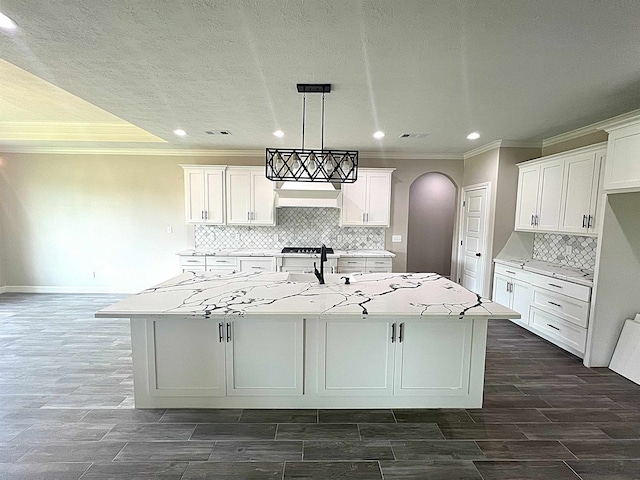 kitchen with light stone counters, a kitchen island with sink, white cabinetry, wood tiled floor, and pendant lighting