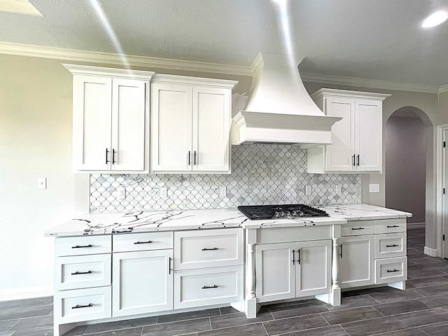 kitchen featuring arched walkways, wood finish floors, white cabinets, custom range hood, and crown molding