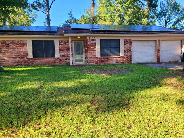 ranch-style home featuring an attached garage, brick siding, solar panels, and a front yard